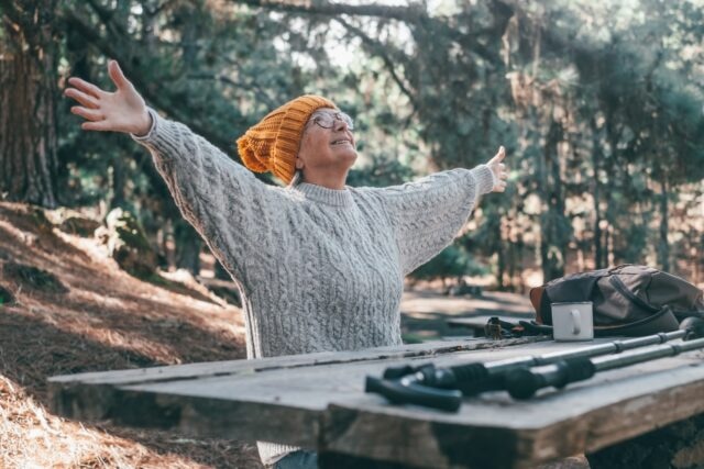 Old woman sitting happily in the forest. Enjoying nature