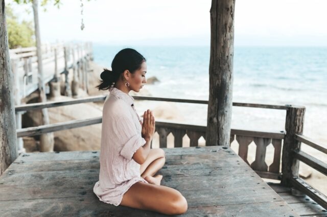 Young woman meditating in a yoga pose in a gazebo at the beach