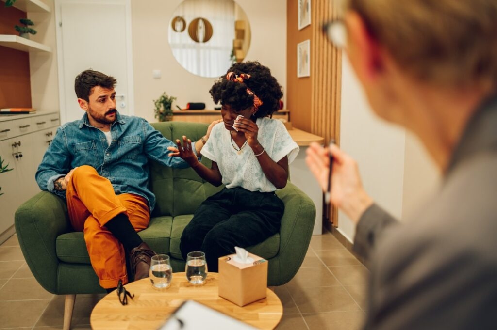 Biracial boyfriend and girlfriend or spouses meeting therapist or counseling psychologist in an office. Diverse couple finding solution to relationship problem. African american woman crying.
