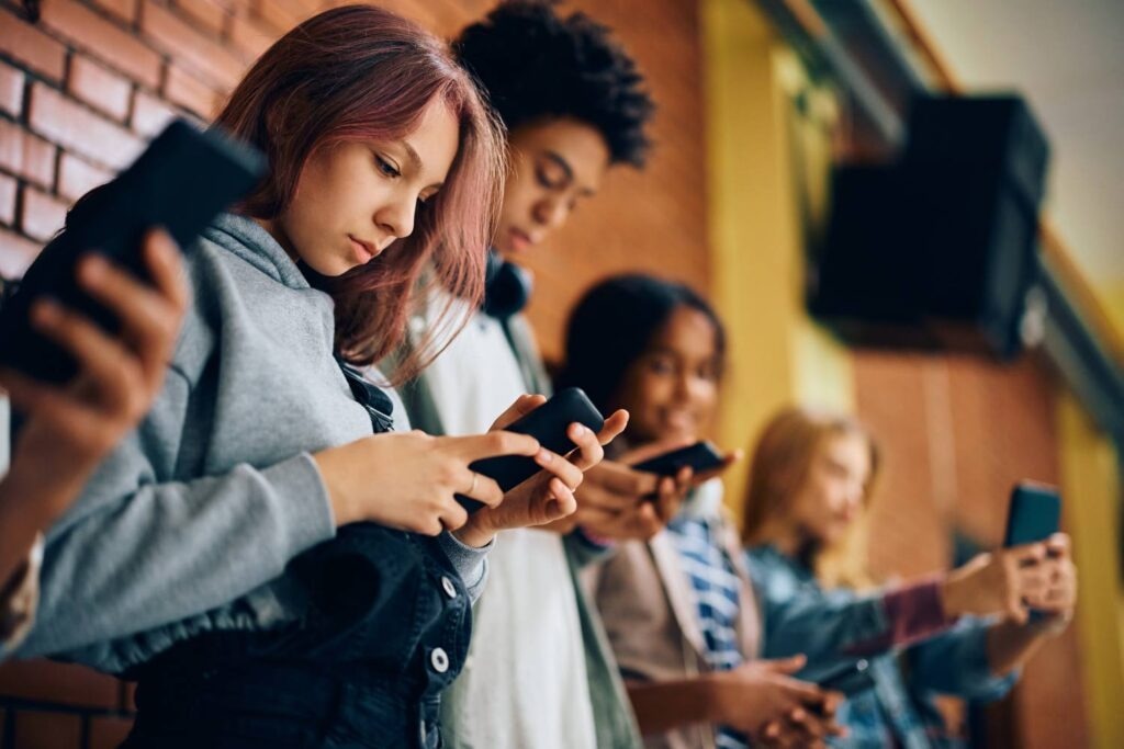 Group of teenagers using mobile phones in hallway at high school