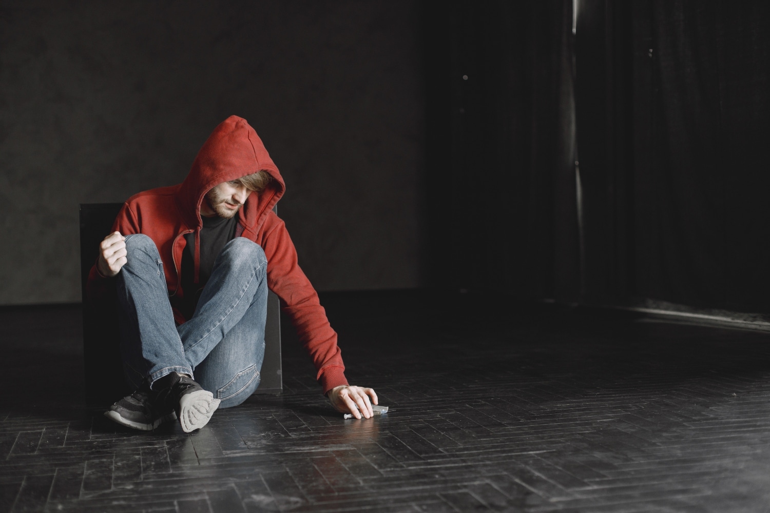 Young man in red sweater. Addicted to drugs, sitting alone and looking at narcotics.