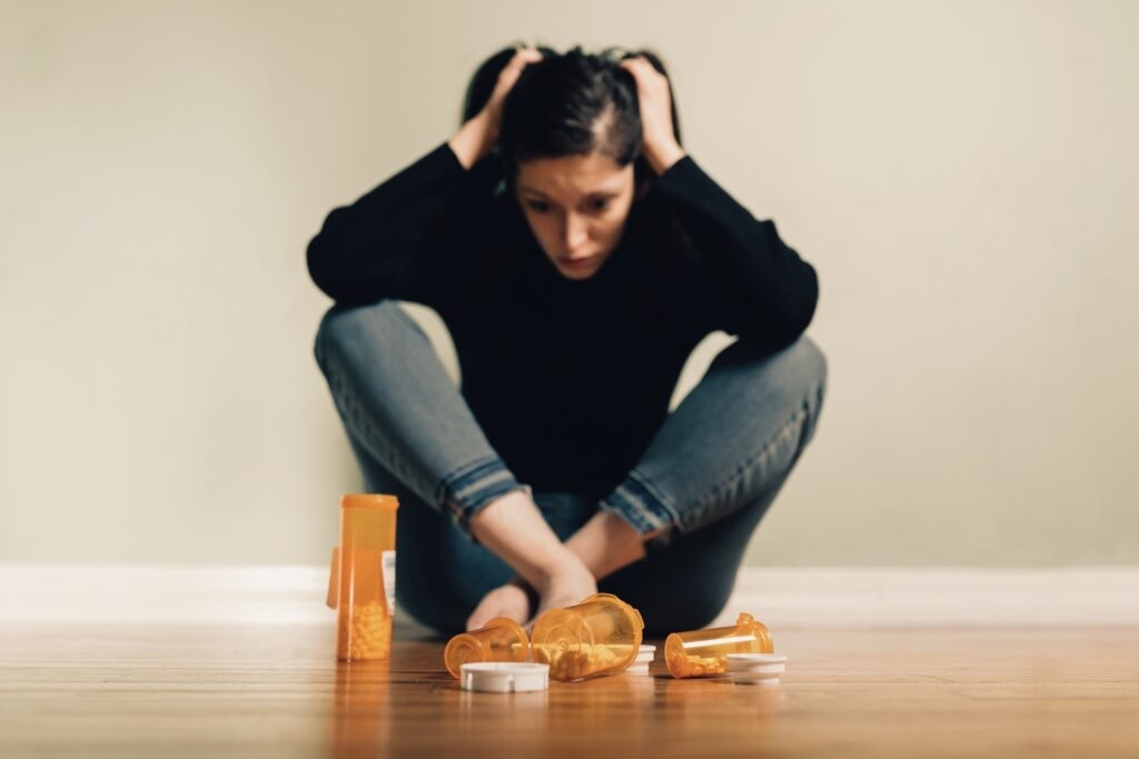 Young millennial woman looking depressed sitting next to a bunch of pill bottles