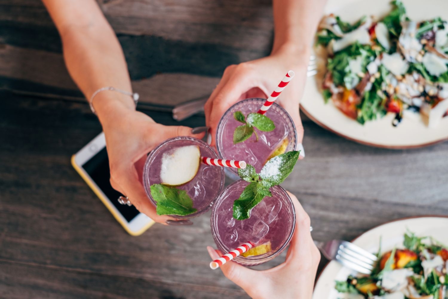 mixed alcohol drinks held by friends over table