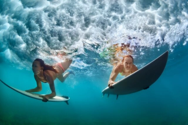 Surfer women with surf board dive underwater under breaking big wave Group of active girls in action. Surfer women with surf board dive underwater under breaking big wave. Healthy lifestyle. Water sport, extreme surfing in adventure camp on family summer beach vacation