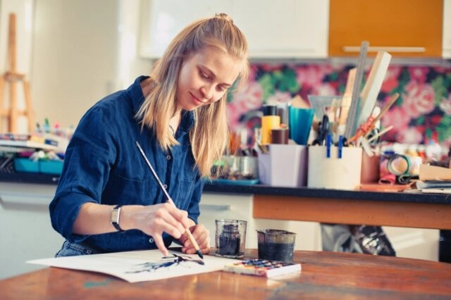 Young Woman Artist Working On Painting In Studio. Selective focus on foreground Young Woman Artist Working On Painting In Studio. Selective focus on foreground