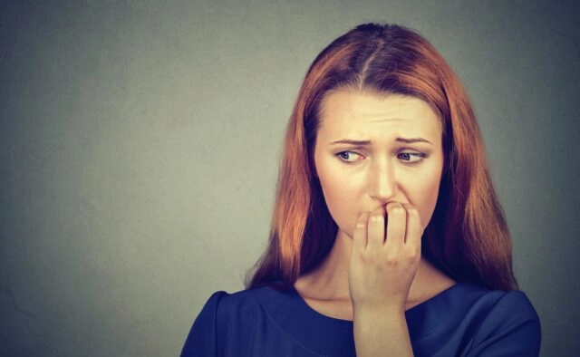 woman thinking while biting nails Closeup portrait young nervous woman biting her fingernails craving something or anxious, isolated on gray wall background. Negative human emotions facial expression feeling