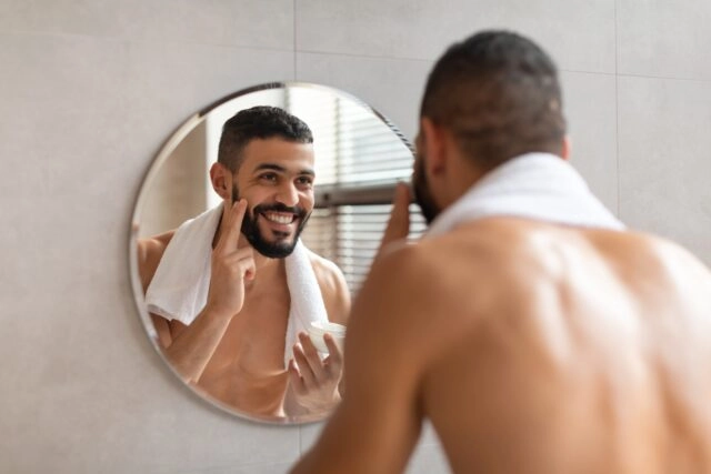 Happy guy looking in the mirror applying cream on face Happy guy looking in the mirror applying cream on face