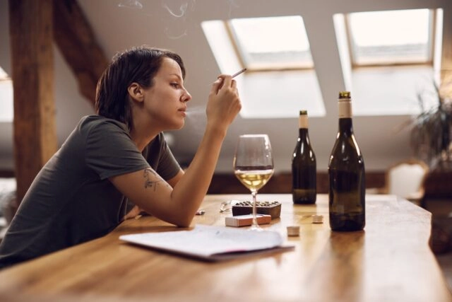Young desperate woman smoking cigarette and drinking alcohol at home Young woman smoking cigarette while suffering from depression and drinking alcohol at home.