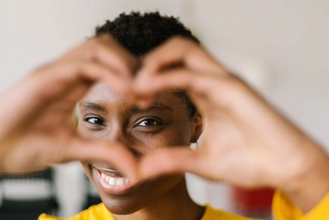 Young smiling lovely multiracial woman showing shape heart with hands and looking through it Young smiling lovely multiracial woman showing shape heart with hands and looking through it