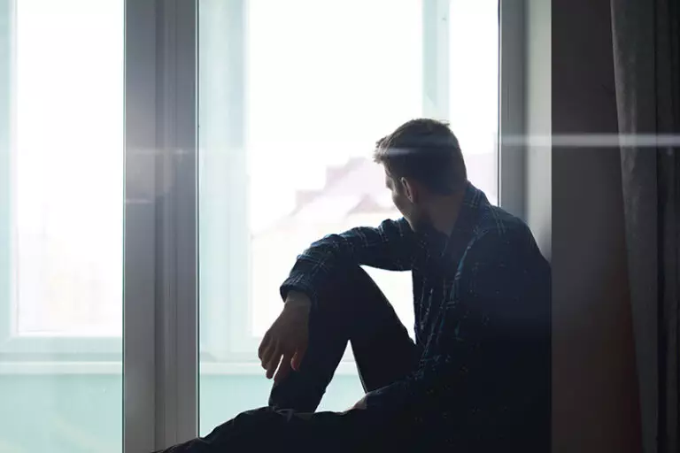 A man struggling with alcoholism and depression looks out a window.