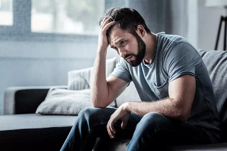 A man going through drug detox sits on a sofa.